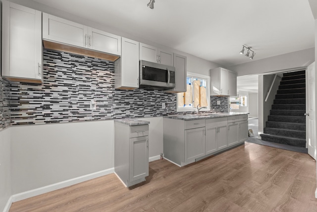 kitchen featuring light wood-style floors, stainless steel microwave, tasteful backsplash, and a sink