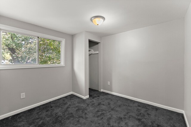 unfurnished bedroom with baseboards, dark carpet, and a closet