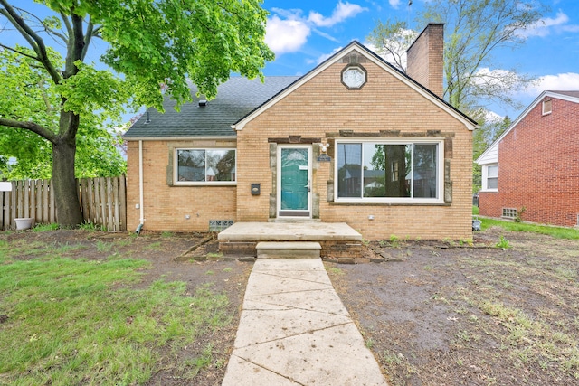 bungalow-style home with a chimney, roof with shingles, brick siding, and fence