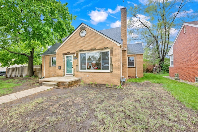 bungalow-style home featuring a chimney, brick siding, a shingled roof, and fence