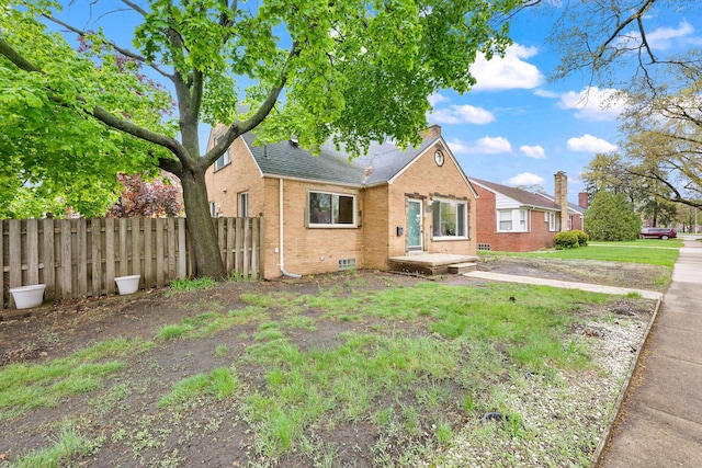 view of front of house with brick siding, roof with shingles, fence, and a front yard