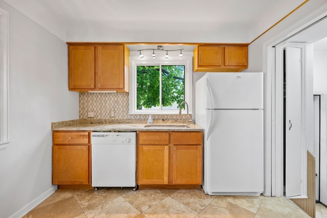 kitchen featuring a sink, brown cabinetry, white appliances, light stone counters, and backsplash