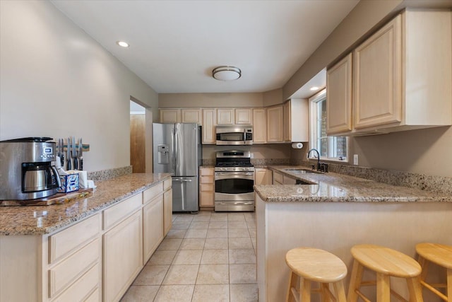 kitchen featuring a peninsula, light tile patterned floors, a sink, stainless steel appliances, and light stone counters