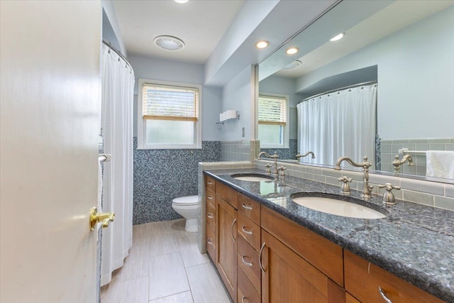 full bathroom featuring toilet, tile walls, double vanity, and a sink