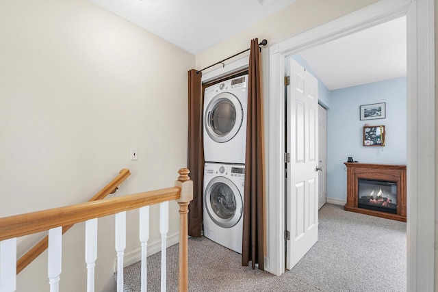 laundry area with stacked washing machine and dryer, light colored carpet, a glass covered fireplace, and baseboards