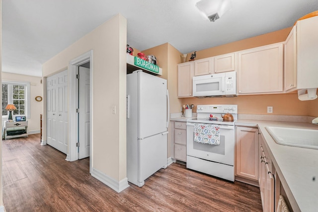 kitchen featuring white appliances, wood finished floors, a sink, light countertops, and baseboards