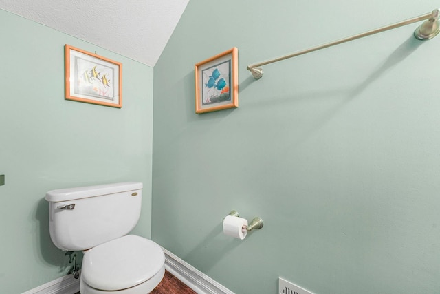 bathroom featuring toilet, a textured ceiling, baseboards, and lofted ceiling