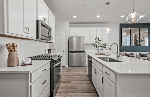 kitchen with stainless steel appliances, a sink, wood finished floors, light countertops, and white cabinets