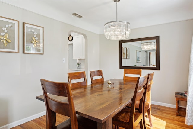 11389 Gold Arbor Rd, Plymouth, MI 48170 - dining area with light wood finished floors, arched walkways, a chandelier, and baseboards