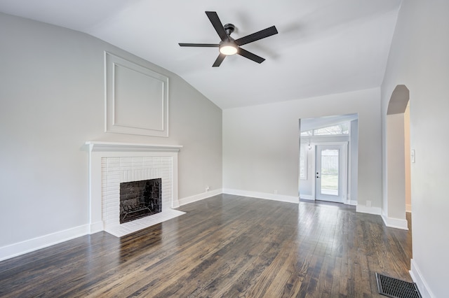 unfurnished living room featuring a ceiling fan, vaulted ceiling, dark wood-style floors, a brick fireplace, and arched walkways