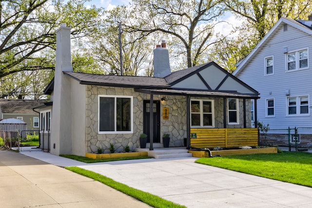 tudor home featuring stone siding, a chimney, a gate, and a shingled roof