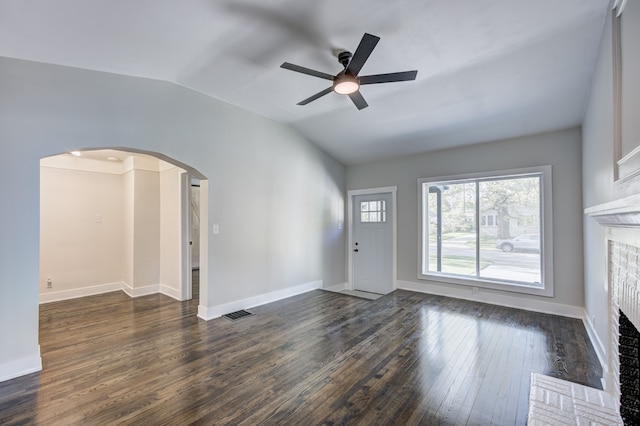 unfurnished living room with arched walkways, lofted ceiling, a brick fireplace, dark wood-type flooring, and a ceiling fan