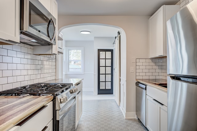 kitchen featuring appliances with stainless steel finishes, arched walkways, white cabinets, and tasteful backsplash