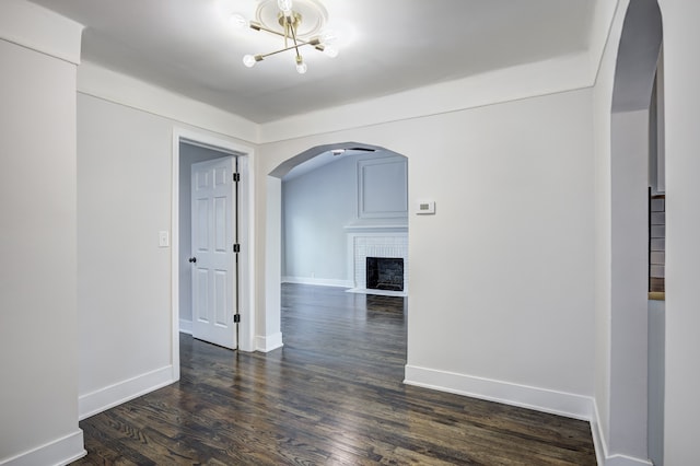 spare room featuring arched walkways, dark wood-style flooring, a brick fireplace, and baseboards