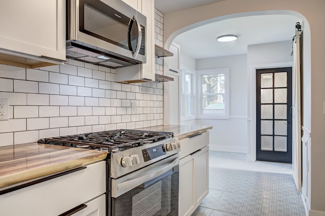 kitchen with stainless steel appliances, arched walkways, white cabinetry, and backsplash