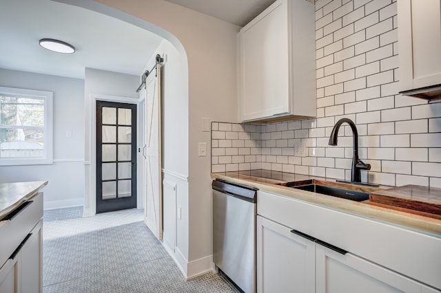 kitchen with stainless steel dishwasher, a barn door, decorative backsplash, white cabinetry, and a sink