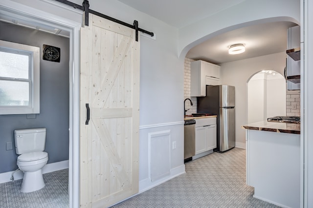 kitchen featuring appliances with stainless steel finishes, a barn door, white cabinetry, backsplash, and arched walkways