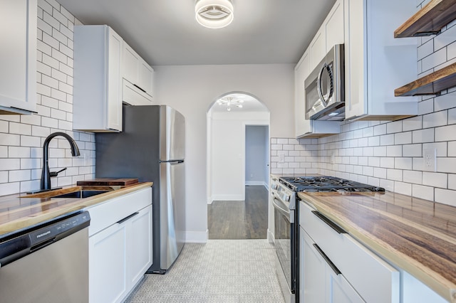 kitchen featuring stainless steel appliances, a sink, open shelves, arched walkways, and white cabinets