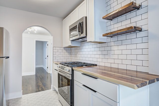 kitchen with stainless steel appliances, arched walkways, open shelves, white cabinetry, and baseboards