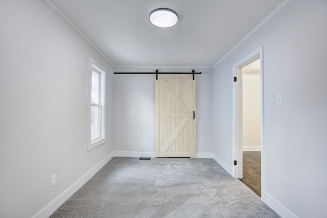 unfurnished bedroom featuring crown molding, a barn door, carpet flooring, and baseboards