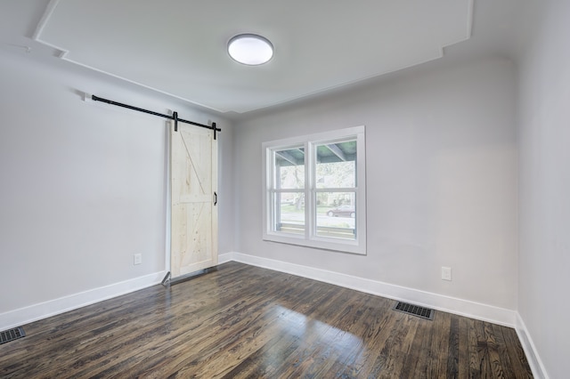 spare room with baseboards, dark wood finished floors, and a barn door