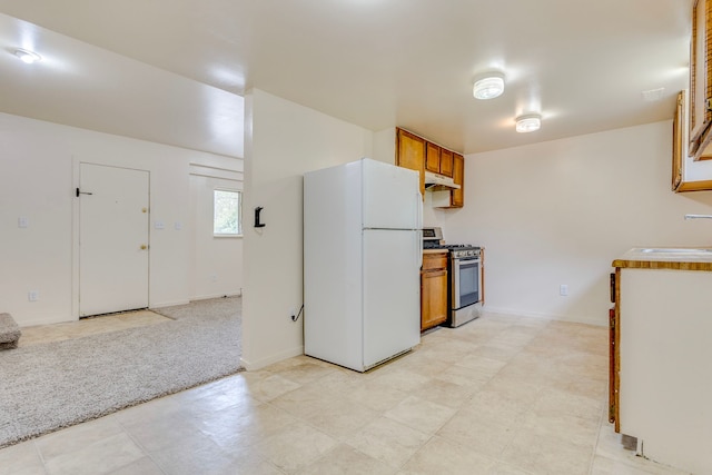 kitchen featuring freestanding refrigerator, stainless steel gas range oven, under cabinet range hood, brown cabinets, and a sink