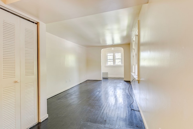 unfurnished living room with arched walkways, dark wood-style floors, and baseboards