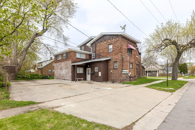 back of house with brick siding, driveway, board and batten siding, and a lawn