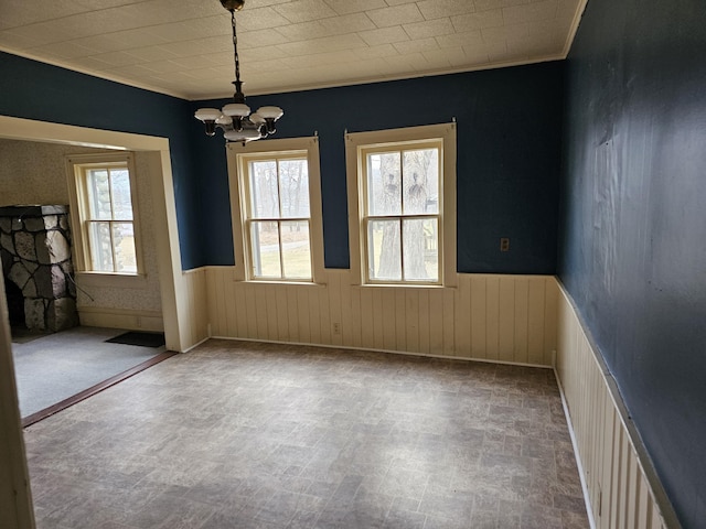 unfurnished dining area featuring a wealth of natural light, a chandelier, crown molding, and a wainscoted wall