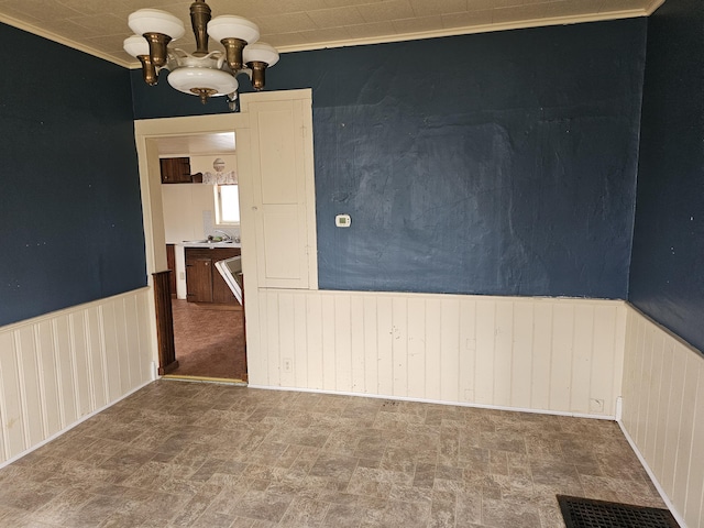 unfurnished room featuring a chandelier, crown molding, and a wainscoted wall