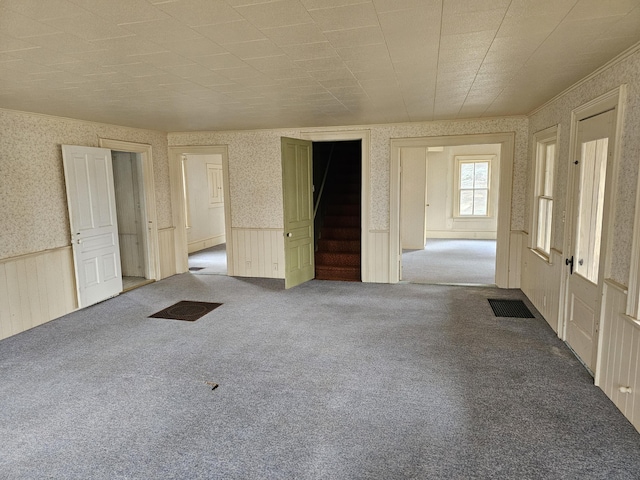 carpeted spare room with stairs, visible vents, wainscoting, and wallpapered walls