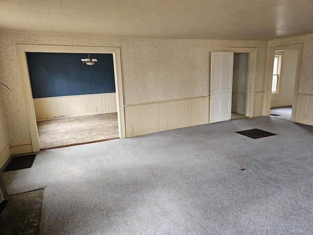 carpeted empty room featuring wallpapered walls, visible vents, and a wainscoted wall