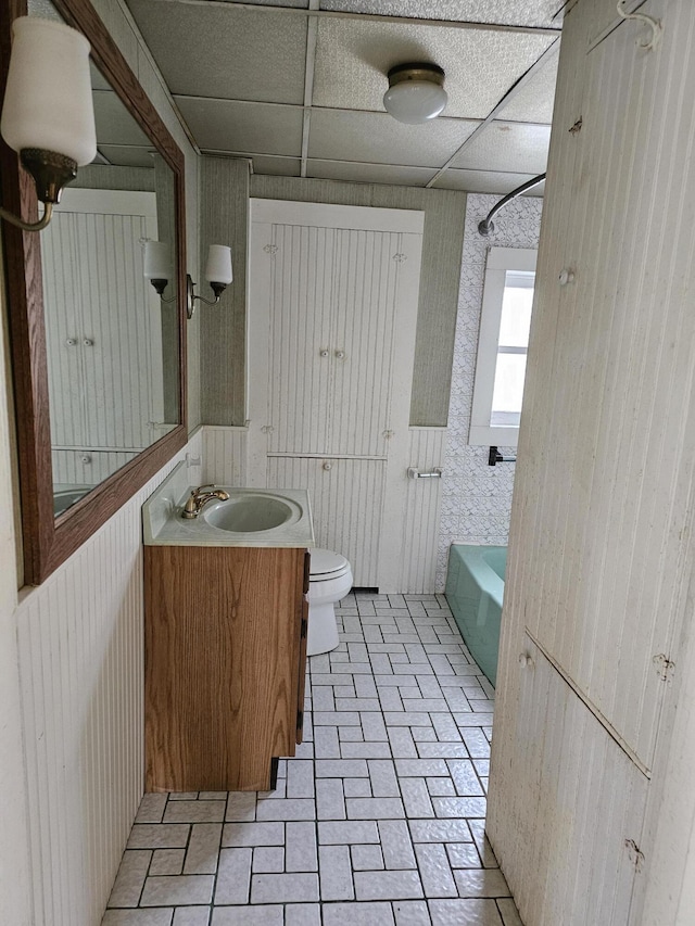 bathroom with toilet, brick floor, vanity, a drop ceiling, and bathtub / shower combination