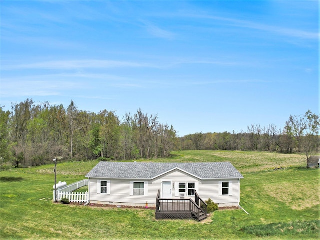 view of front of home with a wooded view, a deck, a front lawn, and roof with shingles