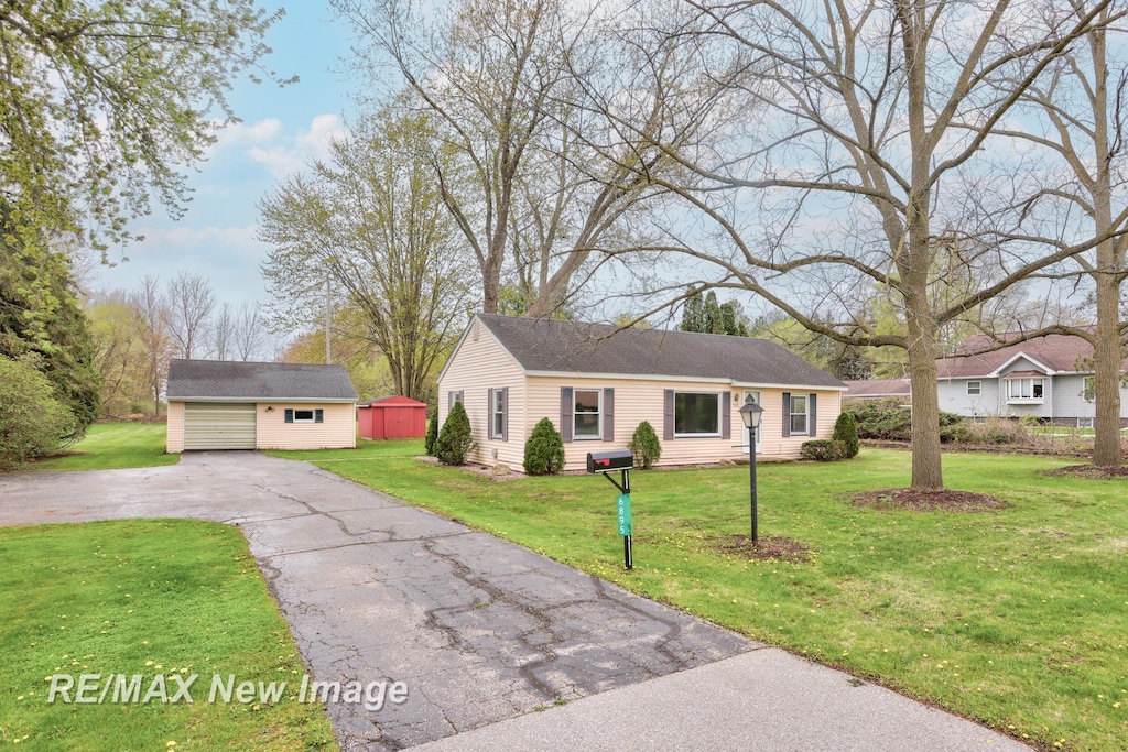 ranch-style house featuring aphalt driveway, a storage shed, a front lawn, and an outbuilding