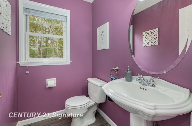 half bath featuring toilet, baseboards, wood finished floors, and a sink