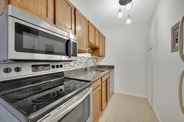 kitchen featuring stainless steel appliances, a sink, backsplash, baseboards, and light tile patterned floors