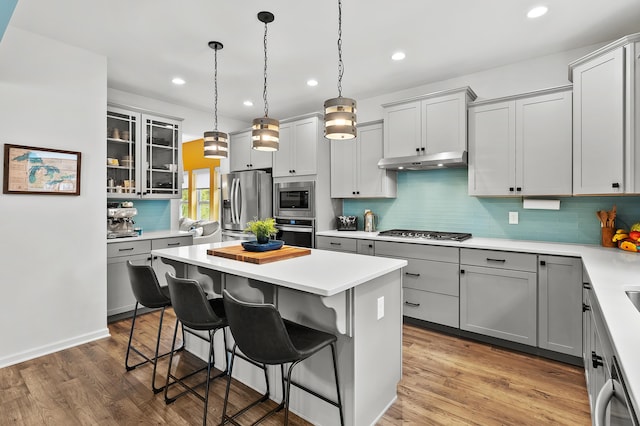 5849 Gavin Ln, Kalamazoo, MI 49009 - kitchen with under cabinet range hood, gray cabinetry, appliances with stainless steel finishes, and a kitchen bar