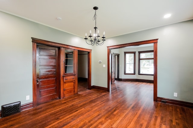 unfurnished dining area with a notable chandelier, baseboards, dark wood-style flooring, ornamental molding, and visible vents
