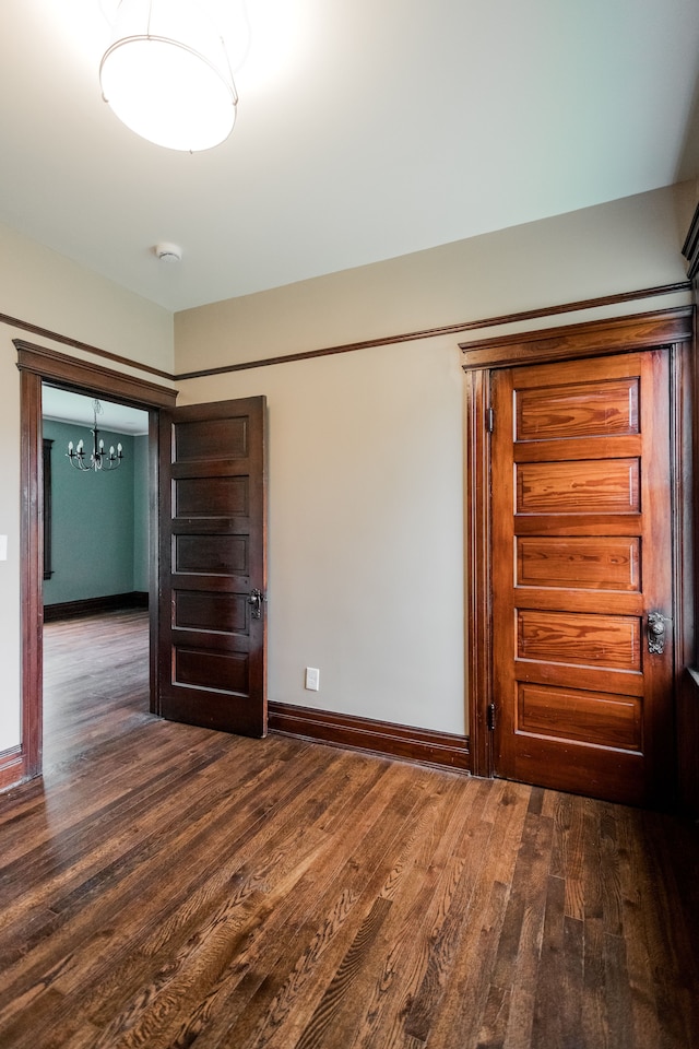 unfurnished bedroom featuring a chandelier, baseboards, and dark wood finished floors