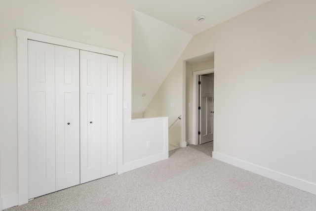 unfurnished bedroom with lofted ceiling, baseboards, a closet, and carpet
