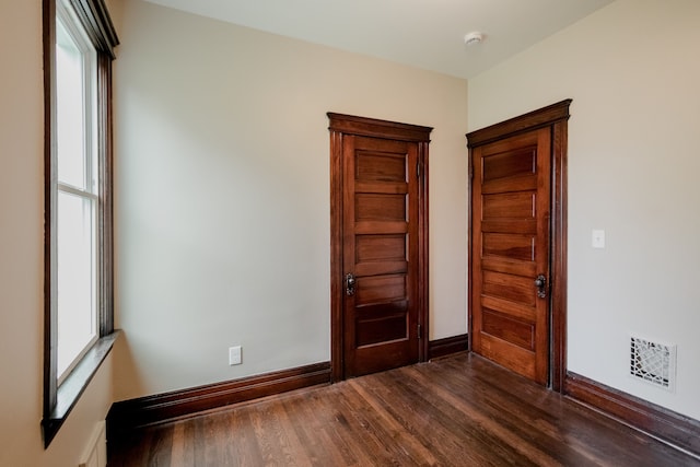 spare room with baseboards, dark wood-style flooring, a healthy amount of sunlight, and visible vents