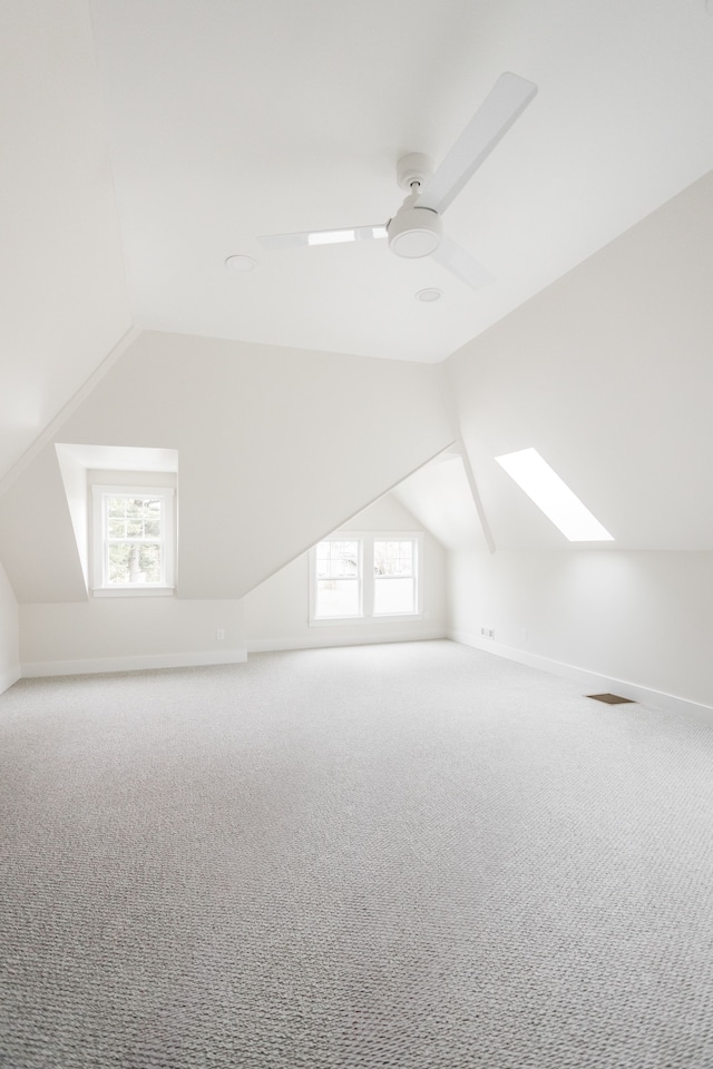 bonus room featuring carpet, baseboards, ceiling fan, and vaulted ceiling with skylight