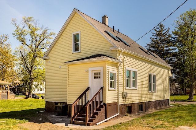 rear view of property with a yard, roof with shingles, entry steps, and a chimney