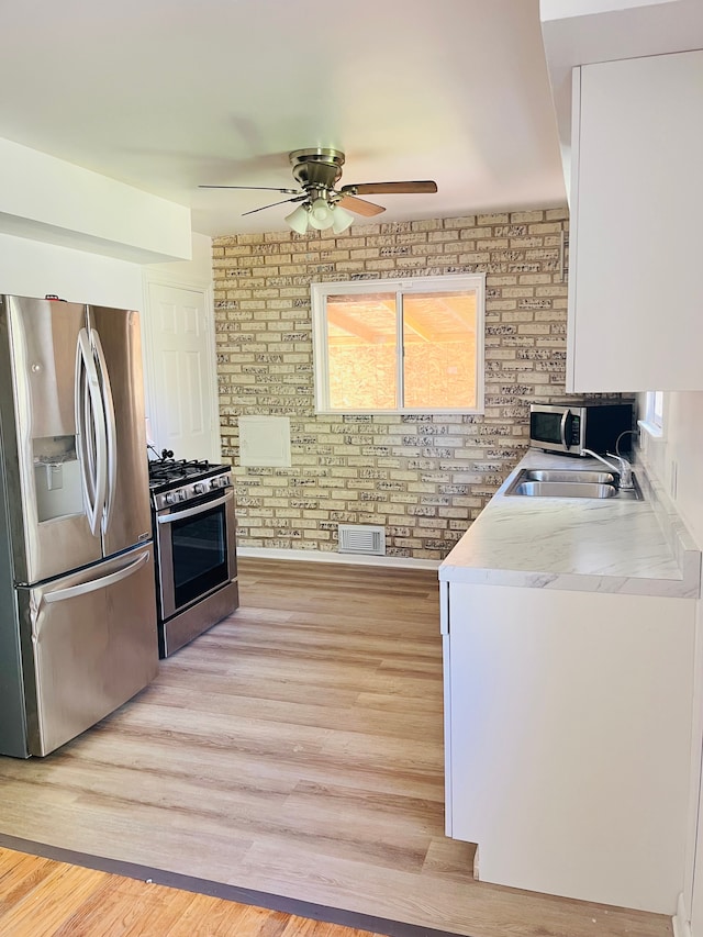 6507 Dupont St, Flint, MI 48505 - kitchen with stainless steel appliances, a ceiling fan, a sink, light wood-style flooring, and brick wall