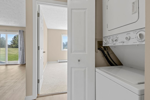 2703 Green Meadows Dr, Traverse City, MI 49685 - clothes washing area with stacked washer and clothes dryer, light wood-style flooring, a baseboard heating unit, a textured ceiling, and baseboards