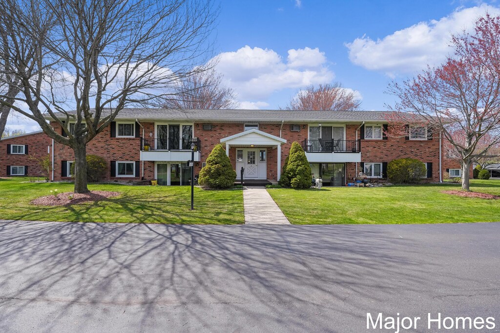 view of property with a front lawn, brick siding, and a balcony