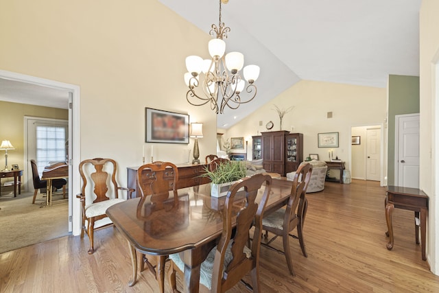 dining area featuring light wood finished floors, a notable chandelier, and high vaulted ceiling