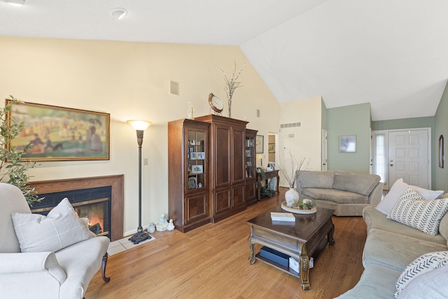 living area featuring light wood-type flooring, a fireplace with flush hearth, visible vents, and high vaulted ceiling