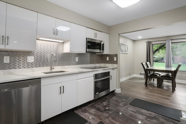 kitchen with appliances with stainless steel finishes, a sink, tasteful backsplash, white cabinetry, and baseboards